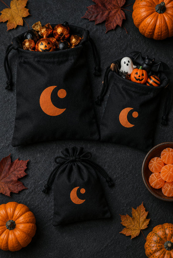 Mustat puuvillaiset kiristysnyöripussit kolmessa koossa oranssilla kuupainatuksella, täynnä Halloween-herkkuja
