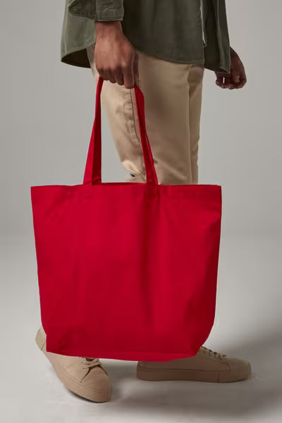 Persona llevando una bolsa maxi de algodón orgánico roja con fuelle por sus asas largas