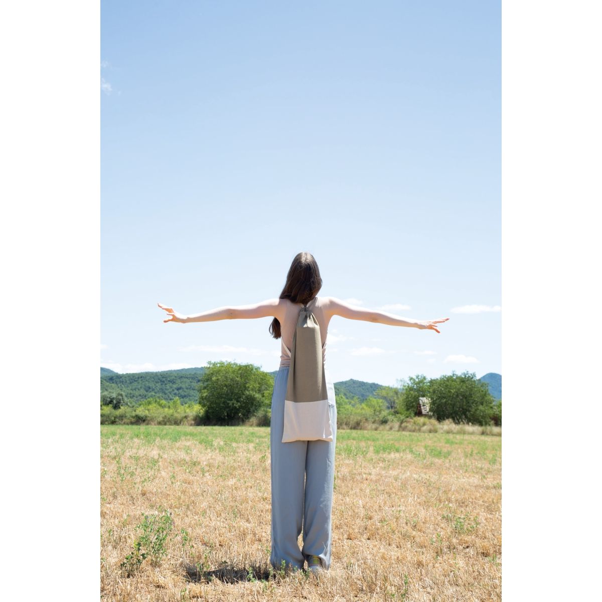 Woman in a field wearing the hemp and natural cotton yoga mat bag on her back